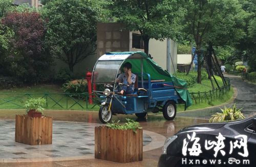 這名快遞哥騎行在小區(qū)通道內(nèi)，一邊接打手機(jī)，一邊還把腳架在車前欄桿上